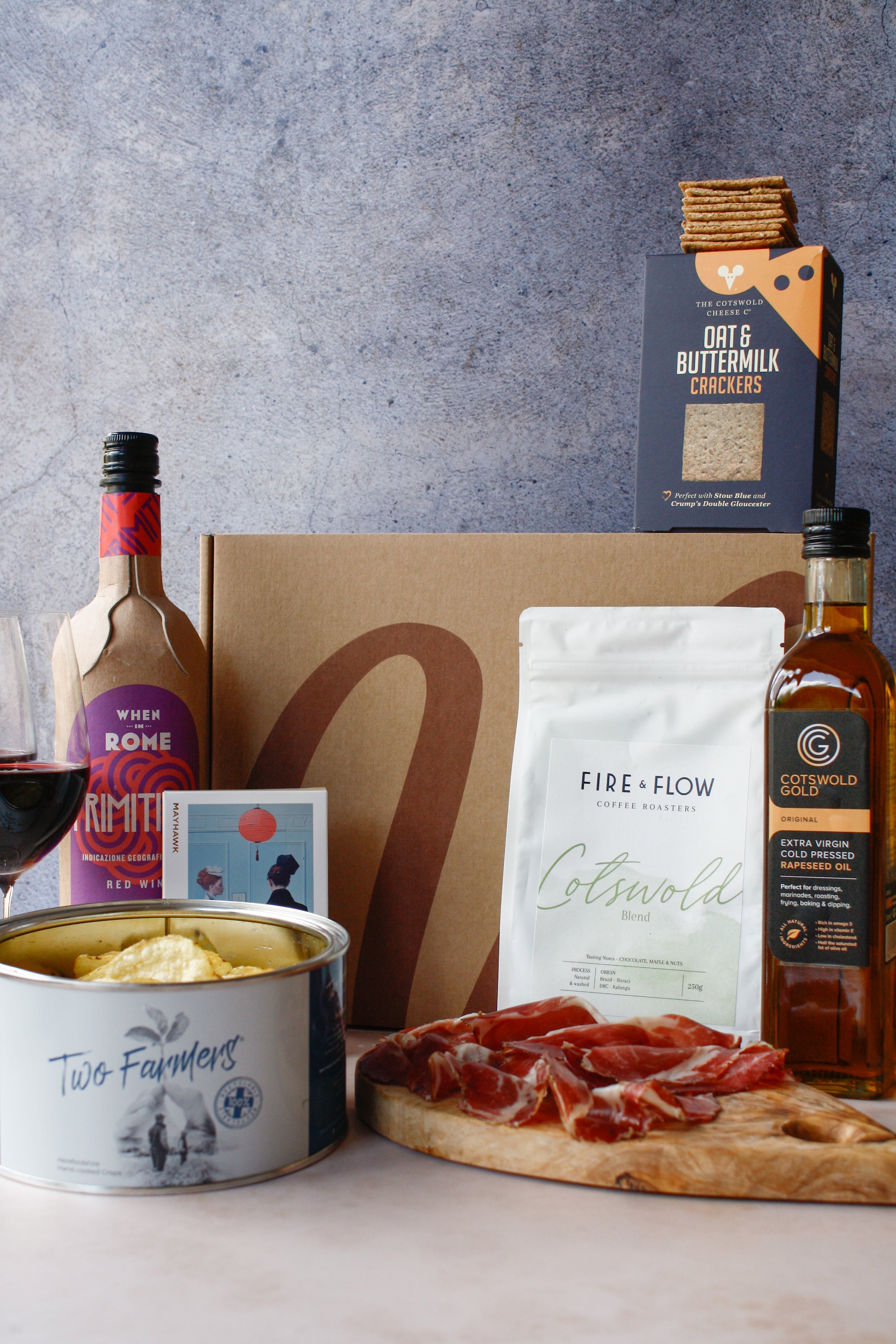 Gourmet food items including a bottle of wine, crackers, cheese, and cured meats on a wooden board with a gray background.