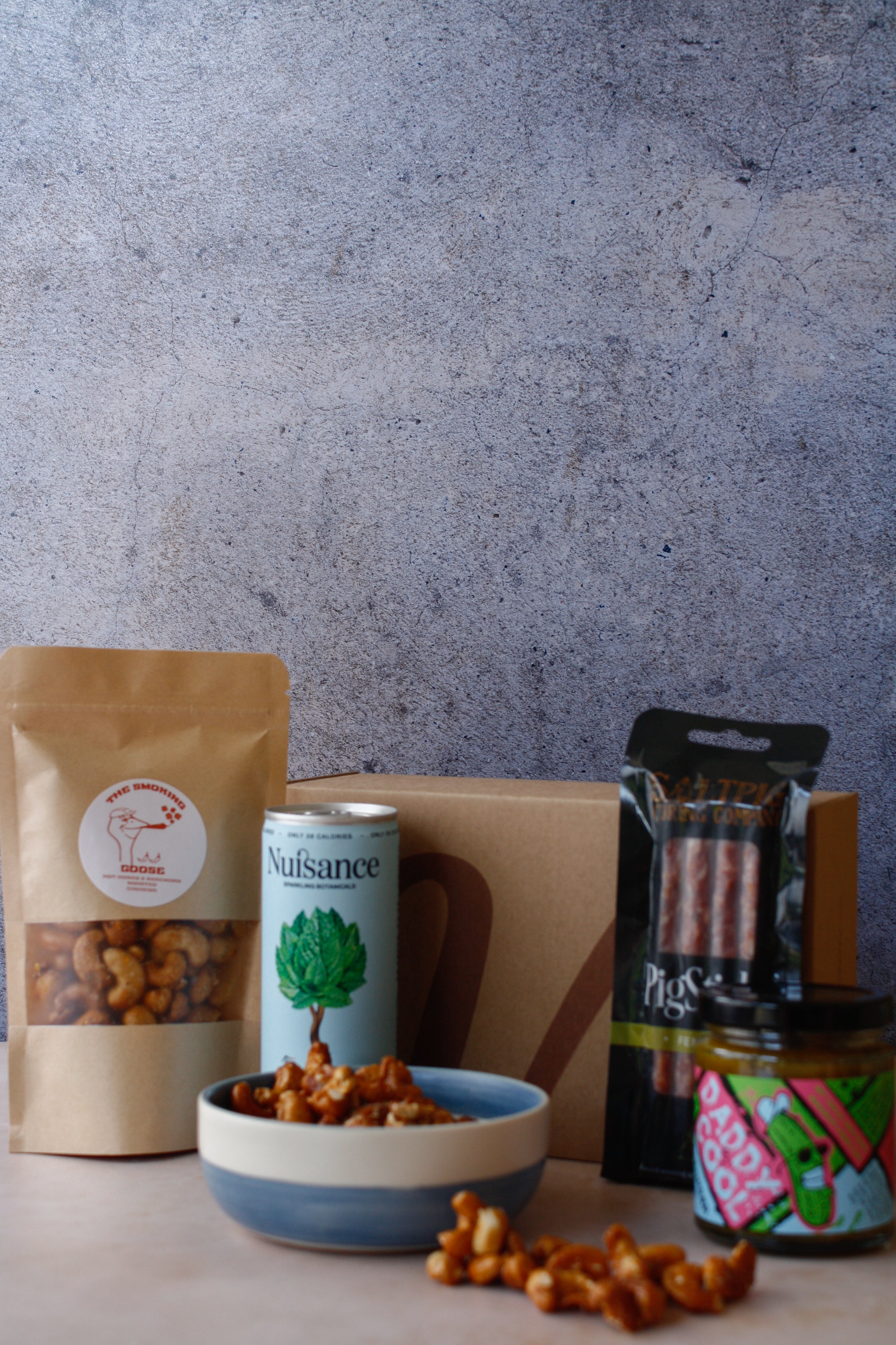 Assorted food items including a bag of nuts, cured meat, a can of drink and jar on a textured surface.
