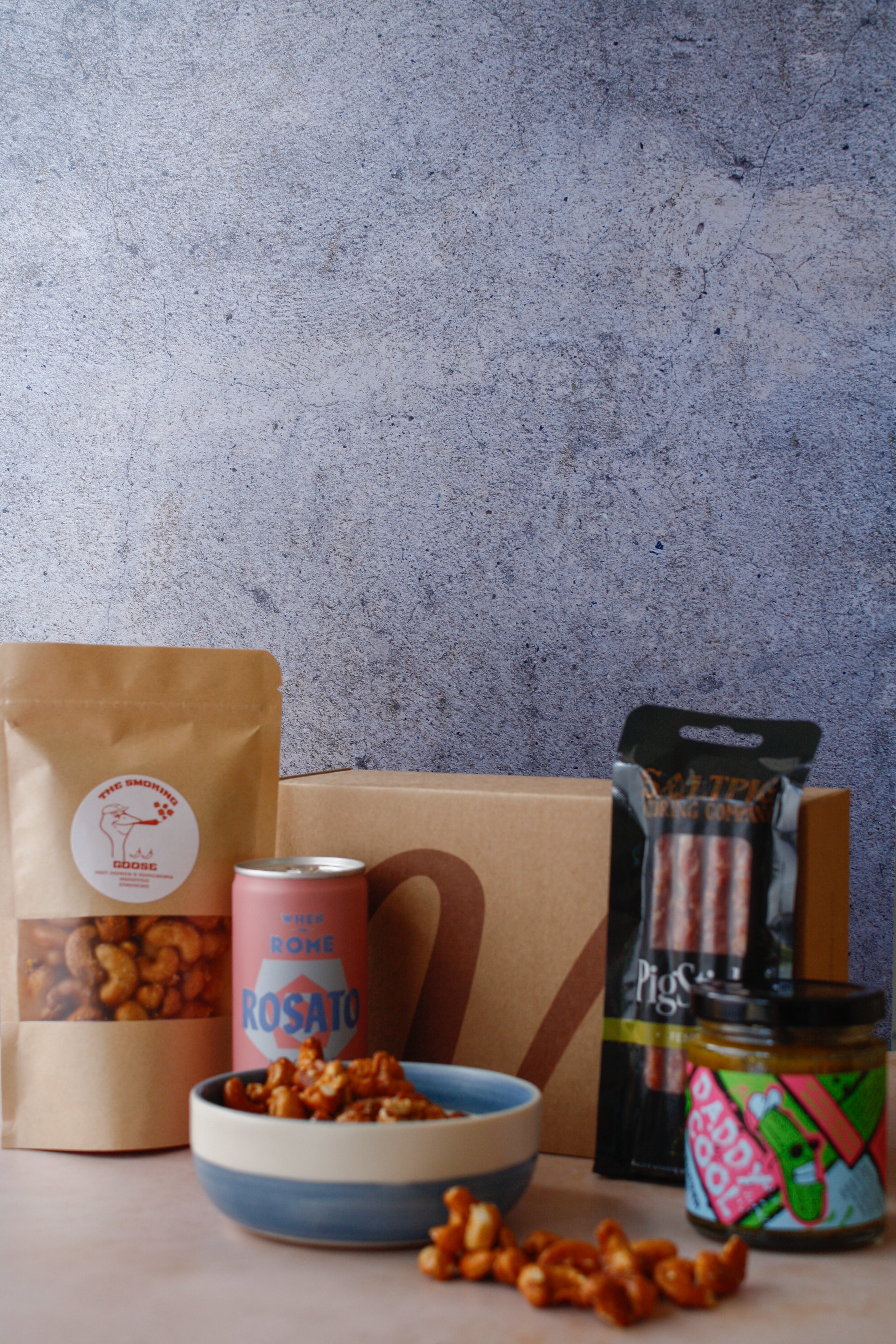 Assorted food items including a bag of nuts, cured meat, a can of drink and jar on a textured surface.