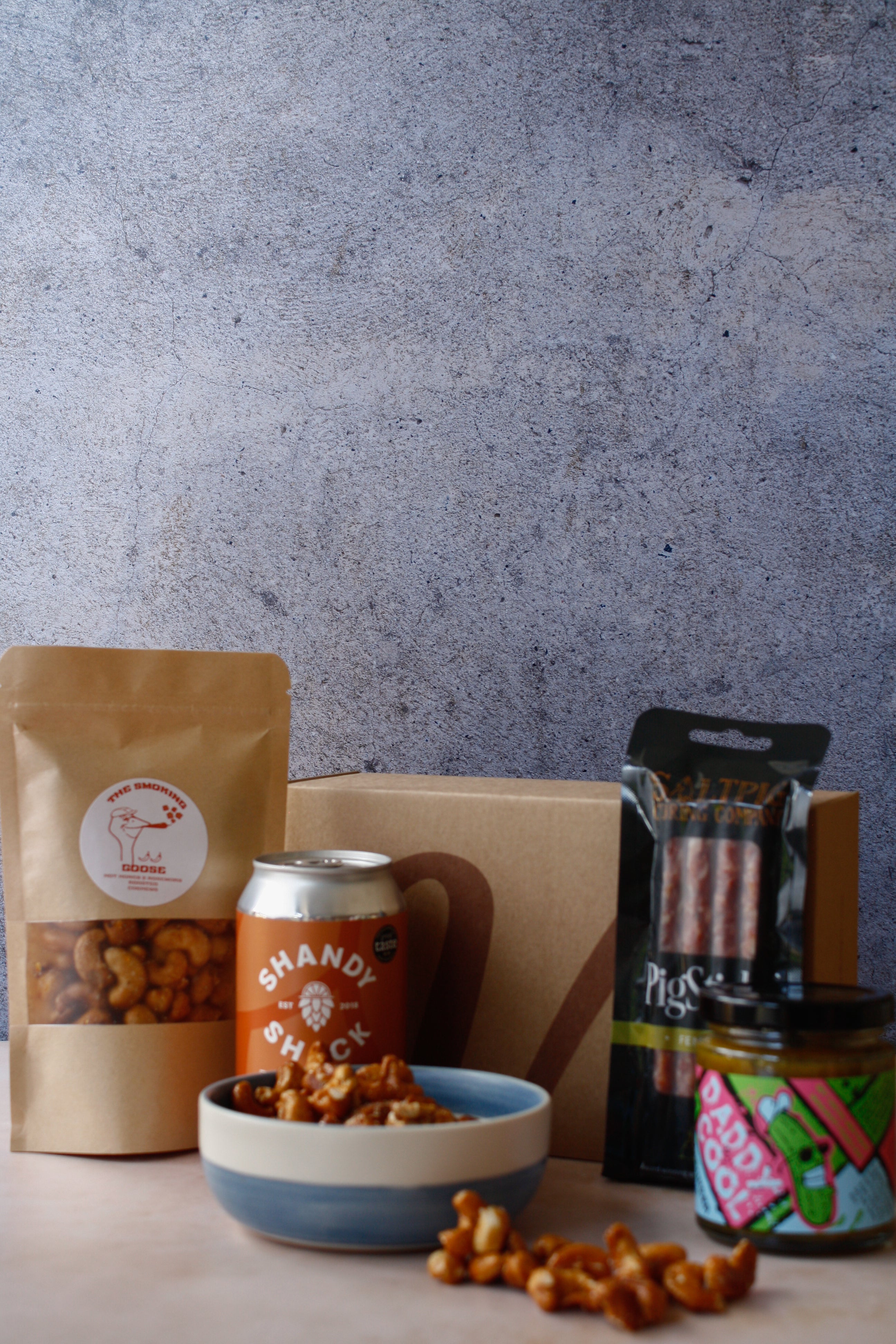 Assorted food items including a bag of nuts, cured meat, a can of drink and jar on a textured surface.
