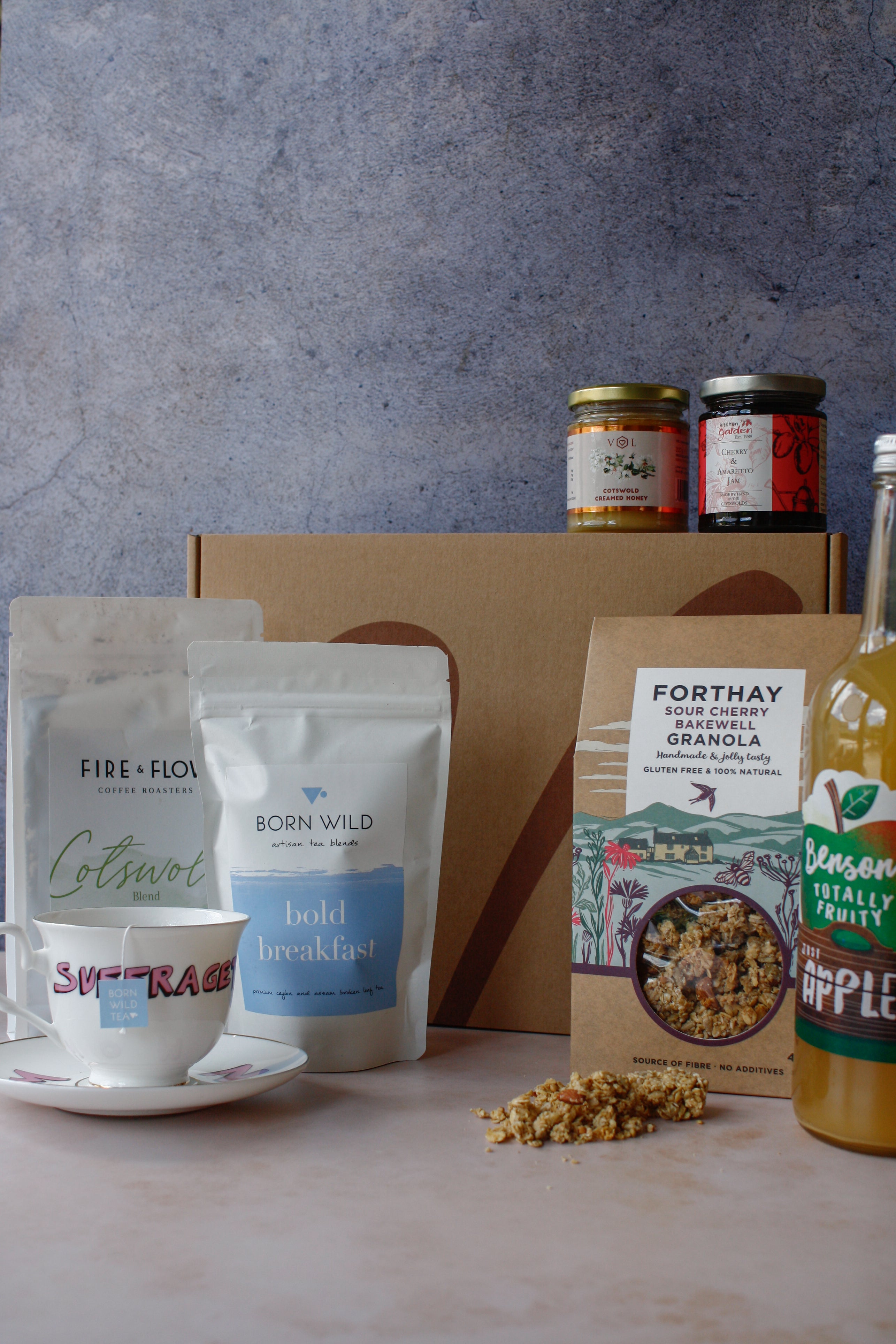 Assorted breakfast items including granola, coffee, tea, apple juice, jam and honey on a marbled surface with a gray background.