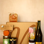 Collection of gourmet items including a bottle, jars, and a box on a beige background