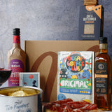 Gourmet food items including a bottle, a can, a box of crackers, and a cutting board with cured meats on a gray surface.