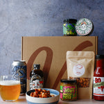 Assorted barbecue food items including a bag of nuts, a can of drink, assorted jars and spice tin on a textured surface.