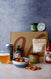 Assorted barbecue food items including a bag of nuts, a can of drink, assorted jars and spice tin on a textured surface.