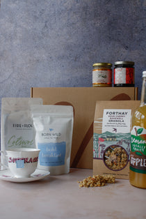 Assorted breakfast items including granola, coffee, tea, apple juice, jam and honey on a marbled surface with a gray background.