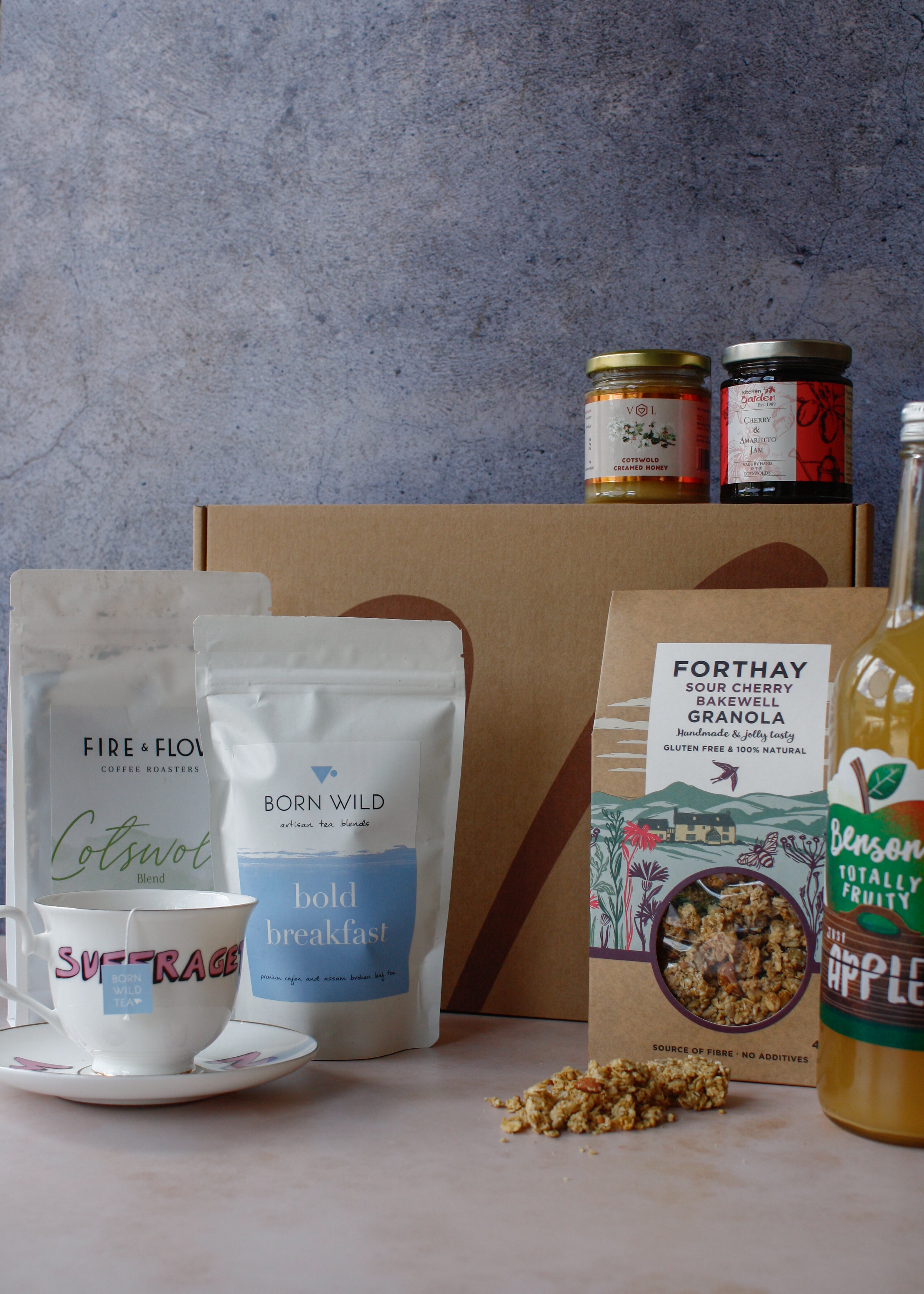 Assorted breakfast items including granola, coffee, tea, apple juice, jam and honey on a marbled surface with a gray background.
