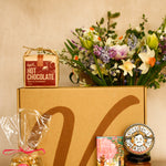 Gift box with hot chocolate, flowers, and other items on a beige background