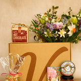 Gift box with hot chocolate, flowers, and other items on a beige background