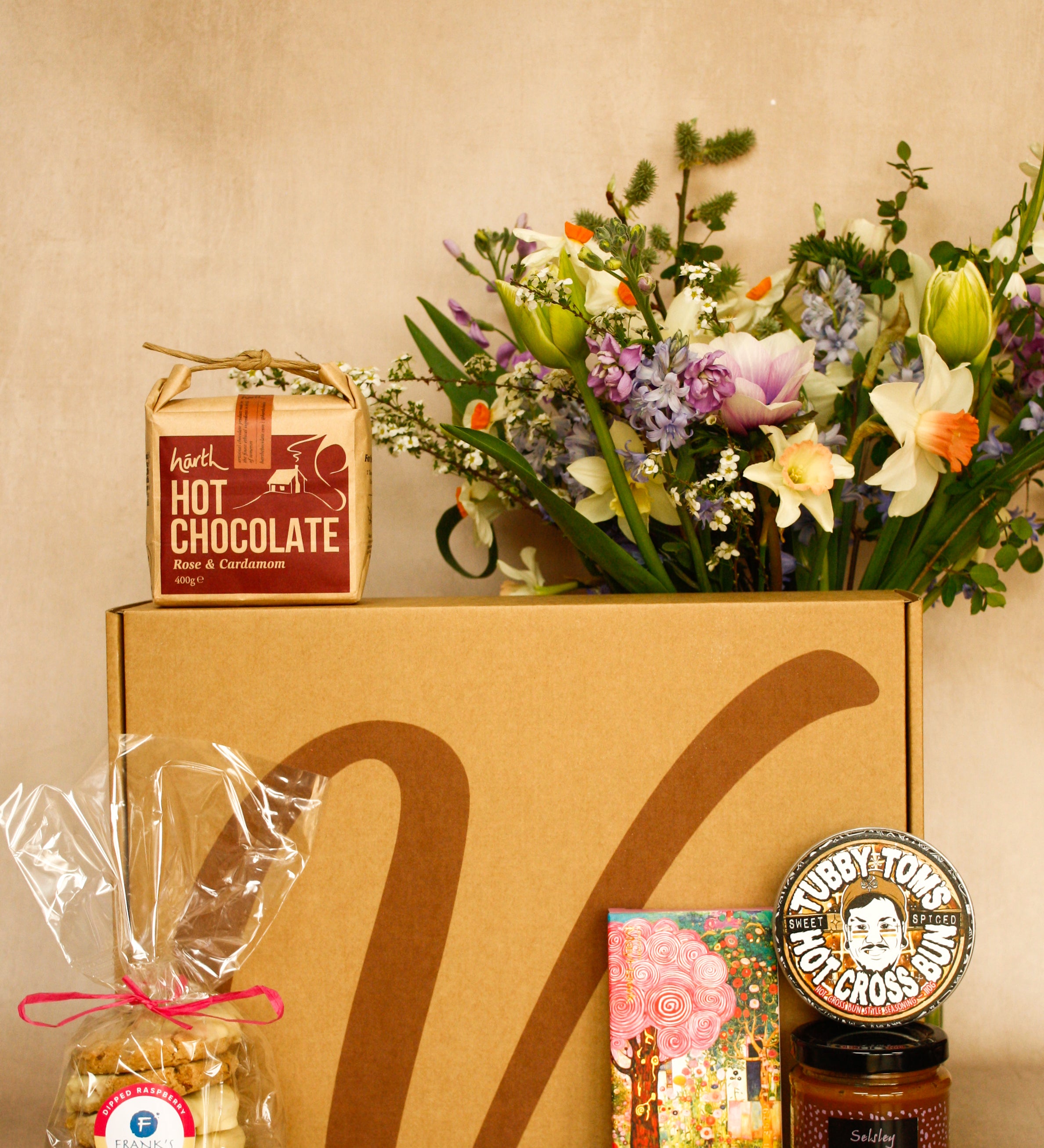 Gift box with hot chocolate, flowers, and other items on a beige background