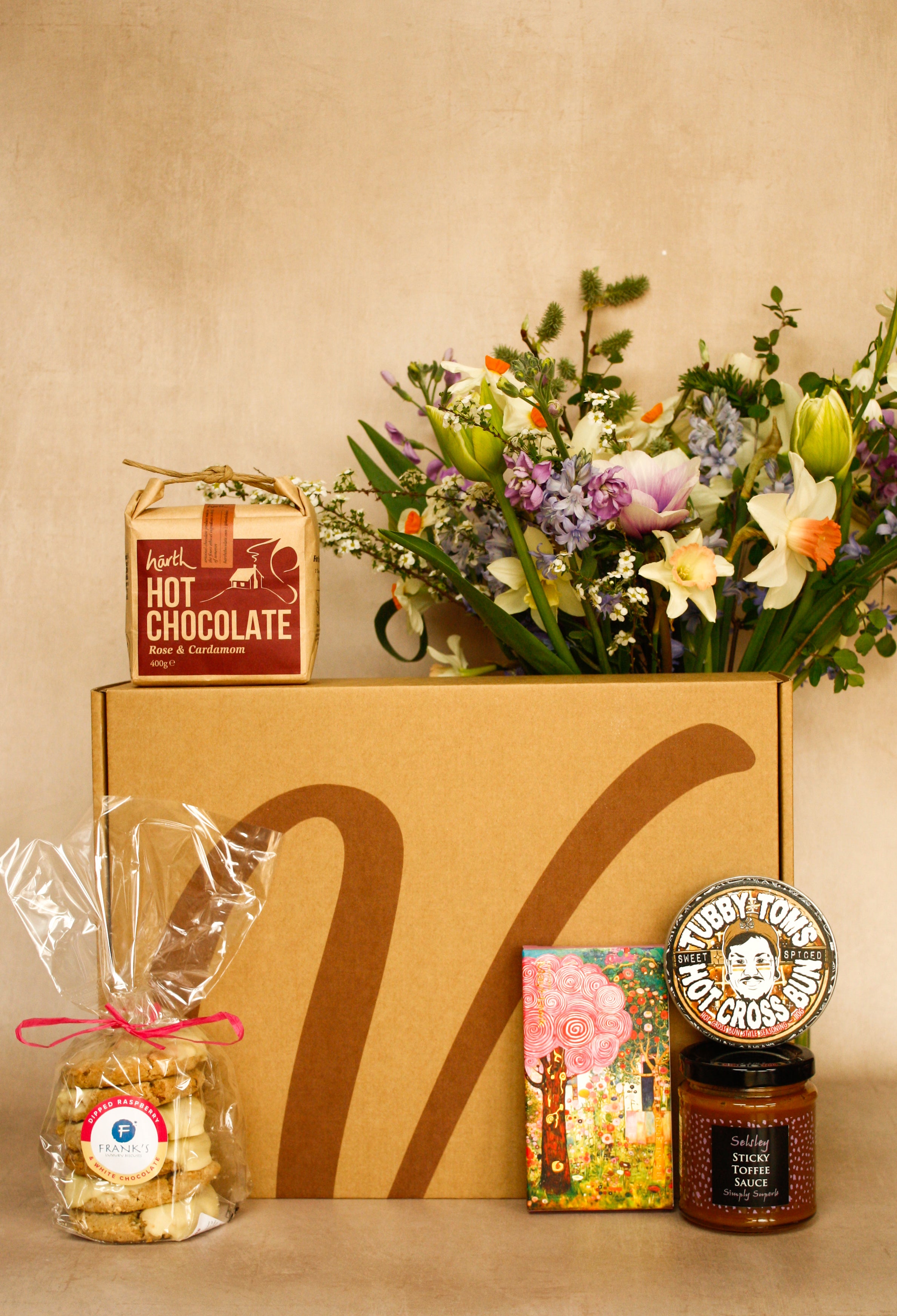 Gift box with hot chocolate, flowers, and other items on a beige background