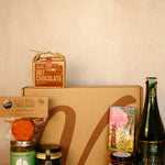 Collection of gourmet items including hot chocolate, cider, and various jars on a beige surface.