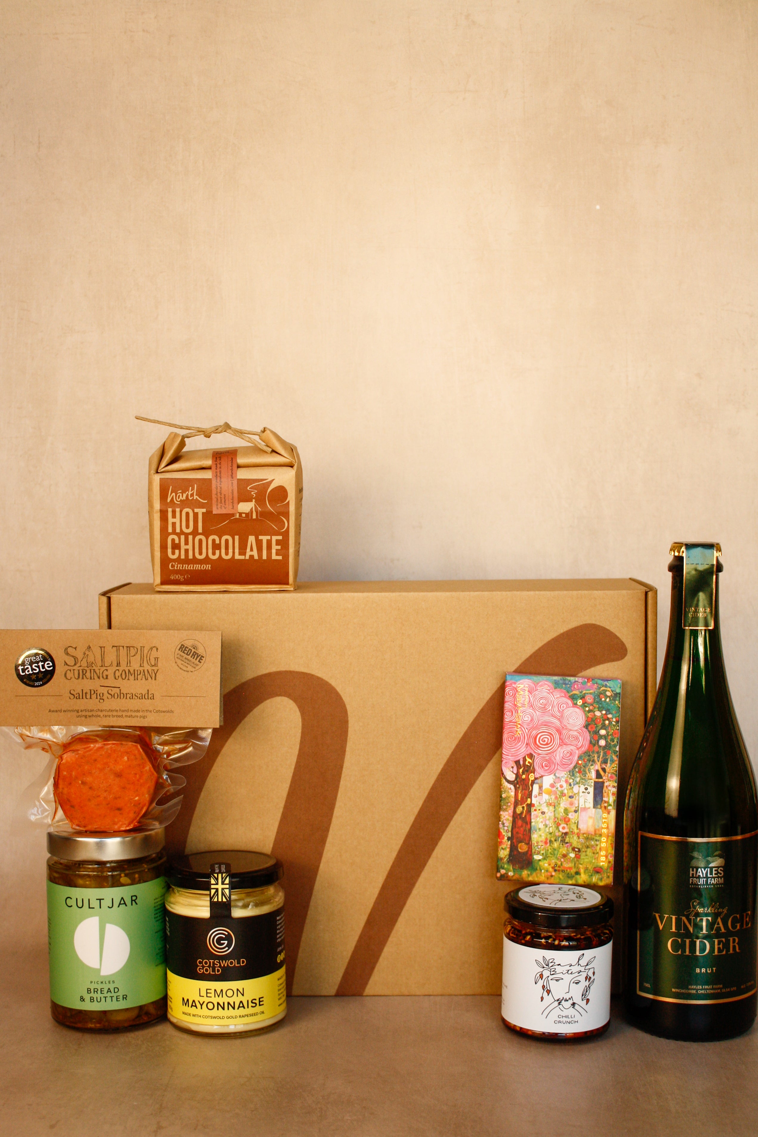 Collection of gourmet items including hot chocolate, cider, and various jars on a beige surface.