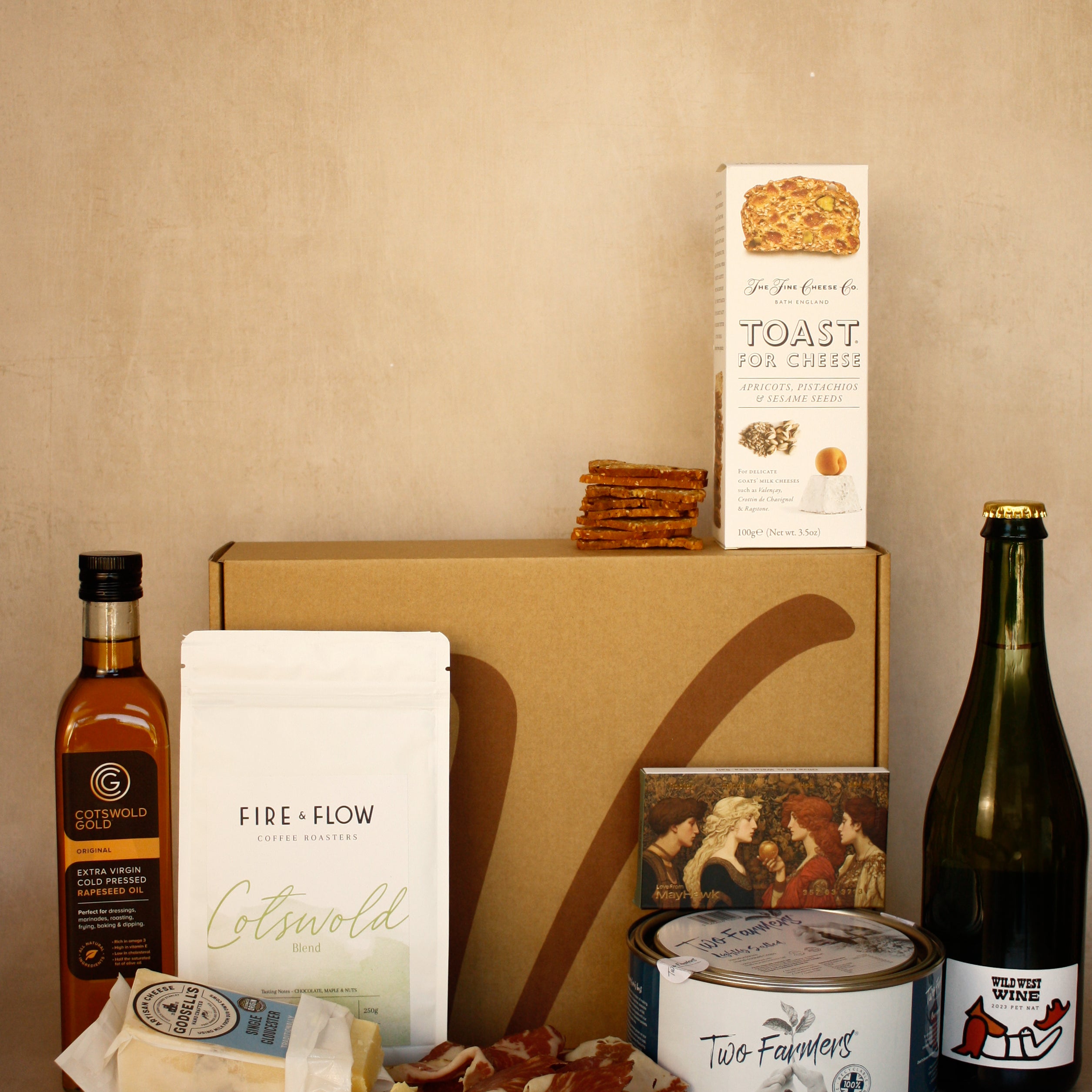 Gourmet food and wine gift set with a box, cheese, wine, and other items on a beige background.