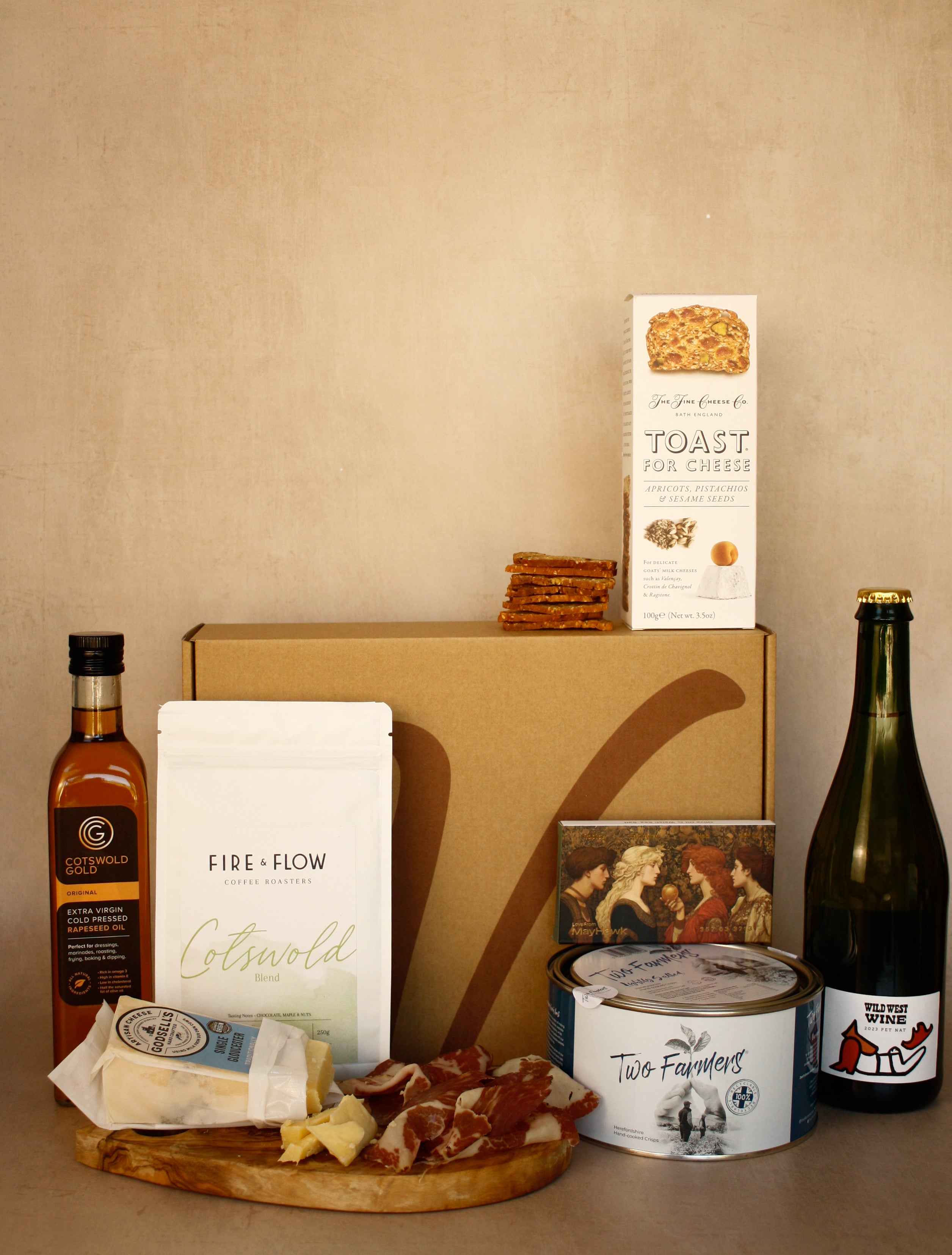 Gourmet food and wine gift set with a box, cheese, wine, and other items on a beige background.